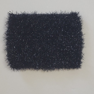 May include: A rectangular, black, fluffy item with a textured surface. The item is set against a white background. The object appears to be a decorative item or a component of a larger craft project.