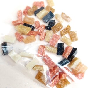 May include: A close-up of a plastic bag filled with small, colorful, rectangular pieces of candy. The candy is in shades of brown, pink, and black.