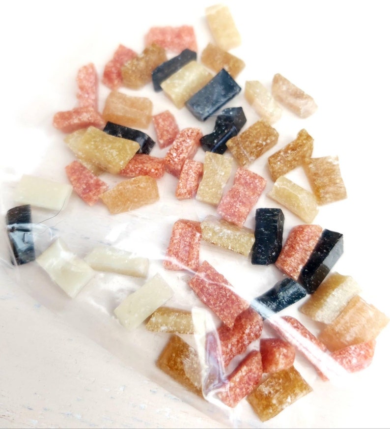 May include: A close-up of a plastic bag filled with small, colorful, rectangular pieces of candy. The candy is in shades of brown, pink, and black.