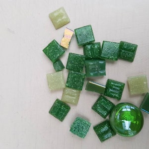 May include: Assortment of green and light green square glass tiles with a round green glass tile.