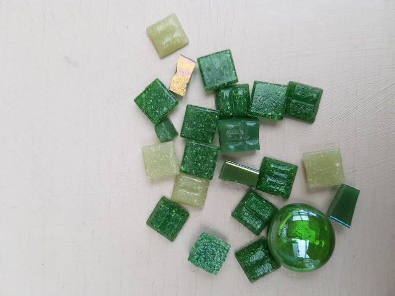 May include: Assortment of green and light green square glass tiles with a round green glass tile.