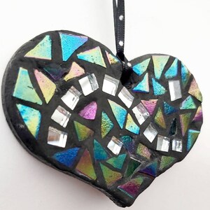 May include: A black heart-shaped ornament with a mosaic design. The mosaic is made of iridescent glass tiles in shades of blue, green, and purple. The ornament has a black ribbon for hanging.