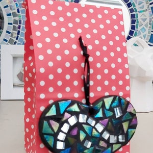 May include: A red and white polka dot gift bag with a black ribbon and a black heart-shaped mosaic ornament hanging from it.
