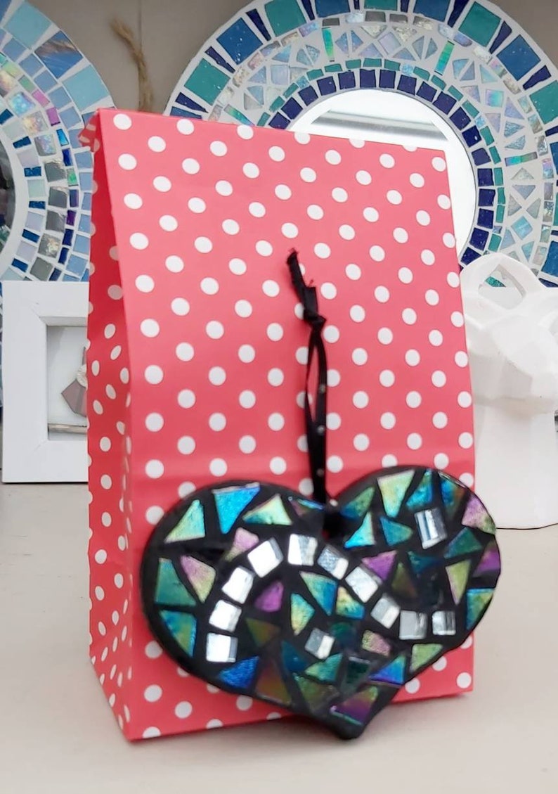 May include: A red and white polka dot gift bag with a black ribbon and a black heart-shaped mosaic ornament hanging from it.