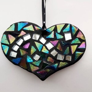 May include: A black heart-shaped ornament with a mosaic design made of iridescent glass tiles. The tiles are arranged in a random pattern and create a colorful and eye-catching effect.