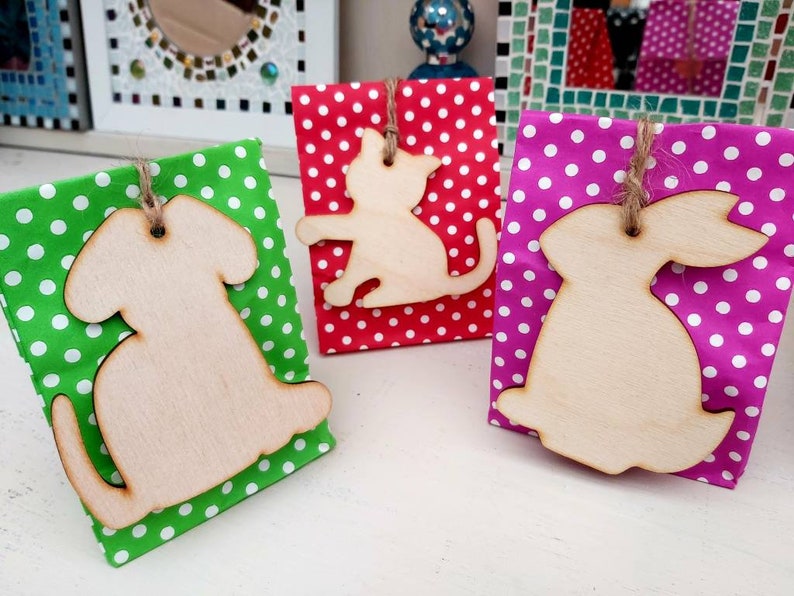 May include: Three gift bags with wooden cutouts of a cat, dog, and rabbit. The bags are decorated with polka dots in red, green, and pink.
