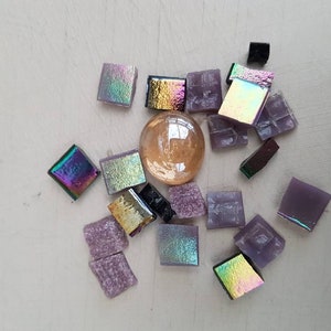May include: Assortment of iridescent and opaque glass mosaic tiles in shades of purple, gold, and black. The tiles are arranged around a clear glass sphere.