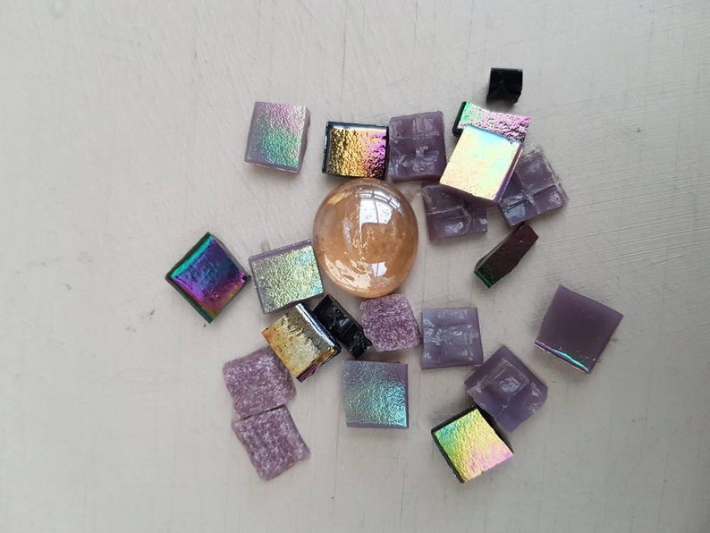 May include: Assortment of iridescent and opaque glass mosaic tiles in shades of purple, gold, and black. The tiles are arranged around a clear glass sphere.