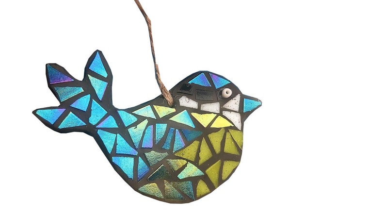 May include: A mosaic bird ornament with iridescent blue, green, and yellow glass pieces. The bird has a dark gray outline and a small white bead for an eye. A brown string is attached for hanging.