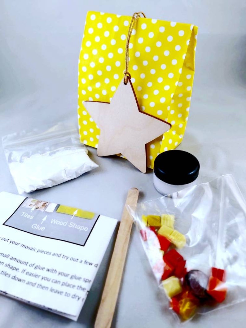 May include: A craft kit for making a mosaic star ornament. The kit includes a wooden star, a bag of colorful mosaic tiles, a small jar of glue, a wooden craft stick, and instructions.