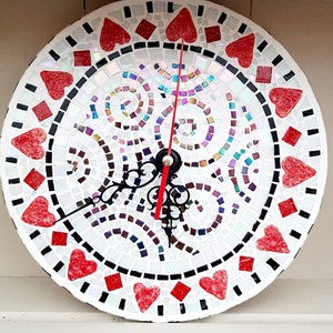 May include: A white mosaic clock with red hearts and black accents. The clock face has a swirling pattern and the hands are black with a red second hand.
