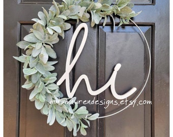 May include: A green leafy wreath with the word "hi" written in white on a metal ring. The wreath is hanging on a black door.