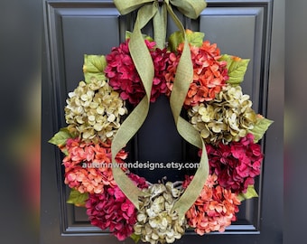 May include: A vibrant wreath featuring a mix of burgundy, orange, and olive green hydrangea blooms. The wreath is adorned with green leaves and a matching green ribbon, perfect for seasonal home decor. The Etsy shop name is visible.