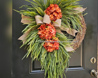May include: A decorative wreath featuring orange hydrangeas and green foliage, accented with a burlap bow. The wreath is made of natural twigs and is designed for a front door. The text "autumnwrendesigns.etsy.com" is visible.