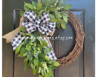 Pode incluir: Uma coroa de ramos marrons com um laço xadrez preto e branco e vegetação. A coroa está pendurada em uma porta preta. O texto "autumnwrendesigns.etsy.com" é visível no laço.