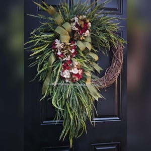 May include: A green and brown wreath with red and white flowers and a green ribbon. The wreath is hanging on a black door.
