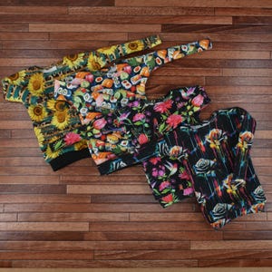 Könnte beinhalten: Vier verschiedene Langarmshirts mit bunten Mustern. Die Shirts zeigen ein Sonnenblumenmuster, ein Sushi-Muster, ein Blumenmuster und ein Schwarzweißmuster mit Rosen und Kolibris.