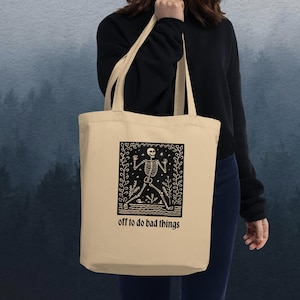 May include: A beige tote bag with a black graphic of a skeleton walking with the text "off to do bad things".