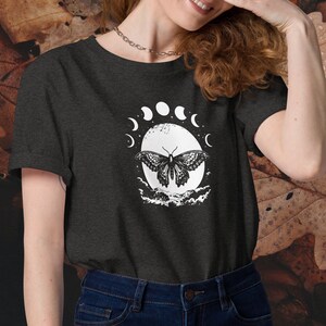 May include: A dark grey t-shirt with a white graphic of a butterfly flying in front of a moon with crescent moons around it.