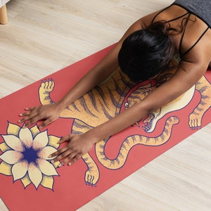 May include: A red yoga mat with a yellow tiger design and a yellow flower with a blue center. A person is doing yoga on the mat.