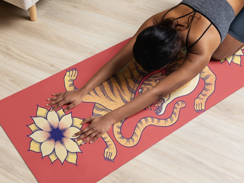 May include: A red yoga mat with a yellow tiger design and a yellow flower with a blue center. A person is doing yoga on the mat.