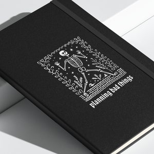 May include: Black notebook with a white skeleton illustration and the text "planning bad things".