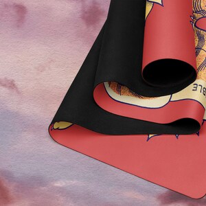 May include: A red yoga mat with a yellow and white floral design and the word "IBLE" printed on the side. The mat is rolled up and the black underside is visible.