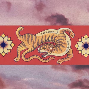 May include: A red background with a stylized orange tiger illustration. The tiger is curled up with the text "STAY FLEXIBLE" and "STAY YOUNG" written on its body. Two yellow flowers with blue centers are on either side of the tiger.