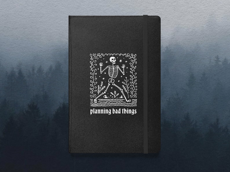May include: Black notebook with a white illustration of a skeleton in a forest setting. The text "planning bad things" is printed below the illustration.