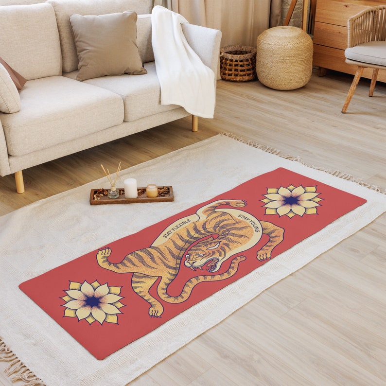 May include: A red yoga mat with a tiger illustration and the text "Stay Flexible" and "Stay Young". The tiger is orange and black with a yellow background. The mat is on a white rug.