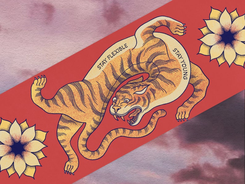 May include: A red background with a stylized illustration of a tiger in a curled position. The tiger is orange and black with a white belly. The text "Stay Flexible" and "Stay Young" is written on the tiger's body. There are two yellow flowers with black centers on the background.