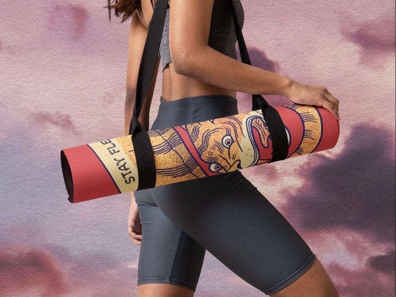 May include: A red and yellow yoga mat with a black strap and the text "Stay Flexy" printed on it. The mat is rolled up and being carried by a person.