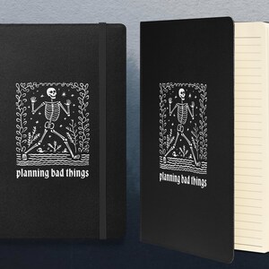 May include: Black notebook with a white skeleton illustration and the text "planning bad things". The notebook has lined pages.