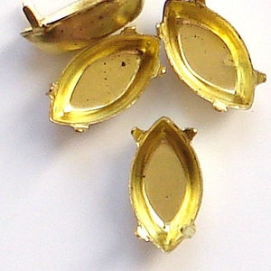 May include: Four gold-colored metal settings for rhinestones or other embellishments. Each setting has a pointed oval shape with a flat bottom and four prongs.
