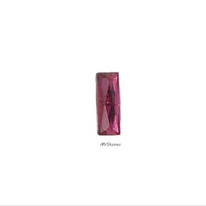 May include: A rectangular, faceted, deep pink gemstone. The gem is set against a white background. The text "MrStones" is in the lower right corner.
