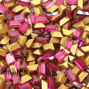 May include: A mix of gold and pink rhinestones. The rhinestones are in various shapes and sizes. The gold rhinestones are pyramid shaped and the pink rhinestones are rectangular.