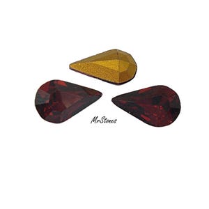 May include: Three teardrop-shaped gemstones. Two are a deep red color, and one is gold. The gold gemstone has a textured, faceted surface. The gemstones are arranged on a white background. The text "Mr. Stones" is in the lower right corner.