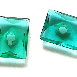 May include: Two square-shaped, teal-colored glass beads with a hole in the center.