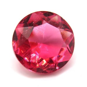 May include: A bright pink, faceted, round gemstone with a high shine.