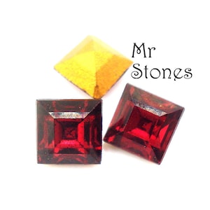 May include: Three square-shaped rhinestones. One is gold, and two are red.
