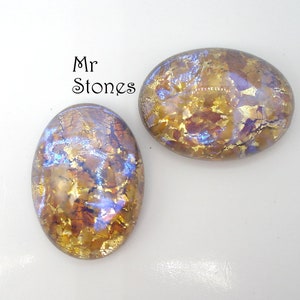 Puede incluir: Dos cabujones de vidrio iridiscente de forma ovalada con un esquema de color dorado y morado. Los cabujones tienen una superficie craquelada y texturizada.