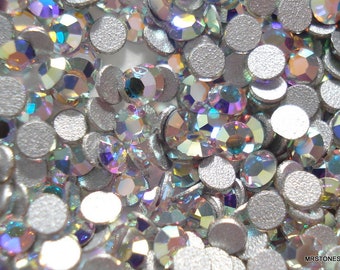 Pode incluir: Uma imagem de close-up de uma grande quantidade de strass de cristal transparente iridiscente. Os strass estão espalhados sobre um fundo prateado.