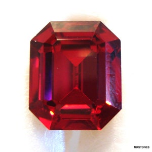 May include: A deep red gemstone with a rectangular emerald cut. The gemstone is faceted and has a high polish.