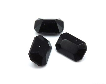 May include: Three black, faceted, rectangular glass gems. The gems are opaque and have a smooth, polished finish.