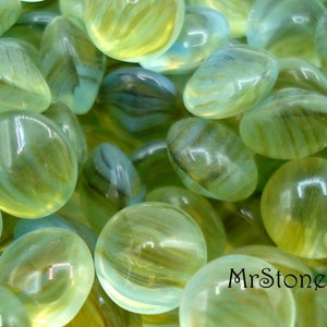May include: A close-up of a group of green and white glass marbles with a swirling pattern. The marbles are smooth and shiny.