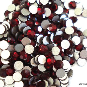 May include: A large pile of small, round, red rhinestones with silver backs. The rhinestones are scattered on a white surface.