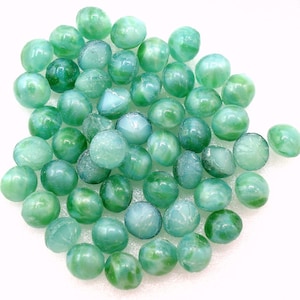 May include: A collection of green glass beads with a swirl pattern. The beads are round and have a smooth, glossy finish.