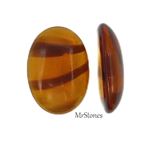 May include: A close-up of two oval-shaped, amber-colored cabochons with brown striations. The cabochons are smooth and polished.