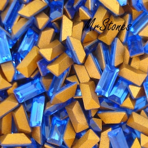 Peut inclure: Une image en gros plan d'un tas de strass en verre bleu et or. Les strass sont en forme de rectangles et de triangles. Le texte "MrStones" est visible sur l'image.