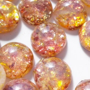 May include: A collection of round, iridescent glass cabochons with a mix of gold and pink hues. The cabochons have a textured, glittery finish.